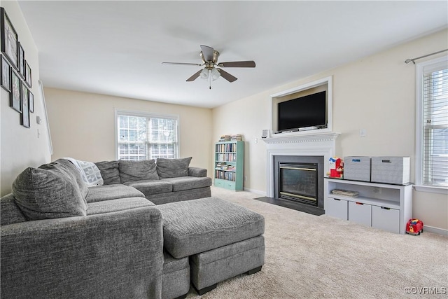 living area with a fireplace with flush hearth, carpet floors, a ceiling fan, and a wealth of natural light