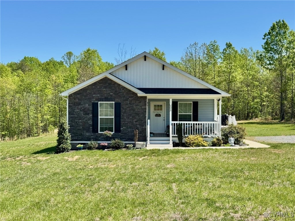 bungalow with covered porch, a wooded view, stone siding, and a front lawn