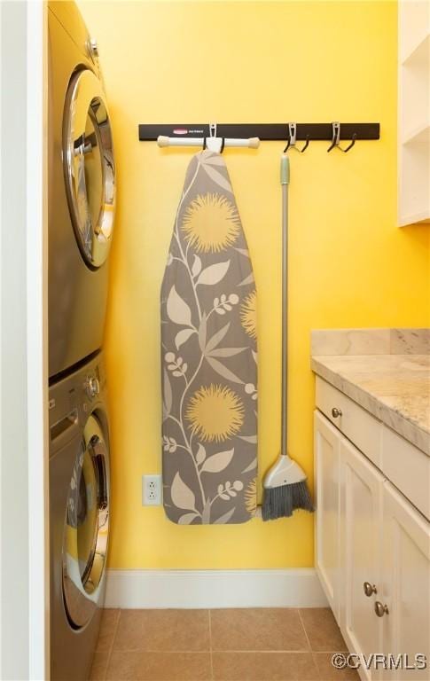 clothes washing area featuring baseboards, stacked washer and clothes dryer, cabinet space, and tile patterned floors