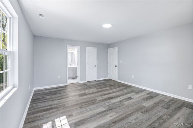 unfurnished bedroom with connected bathroom, baseboards, visible vents, and wood finished floors