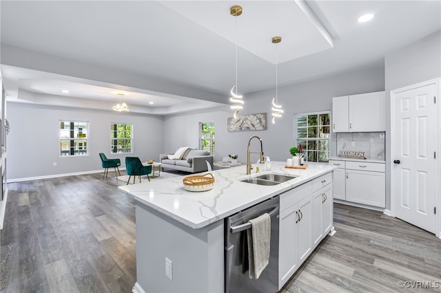 kitchen with a sink, a raised ceiling, open floor plan, and dishwasher