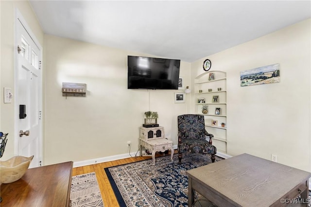 sitting room with baseboards, built in features, and wood finished floors