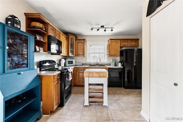 kitchen featuring open shelves, glass insert cabinets, brown cabinets, a sink, and black appliances