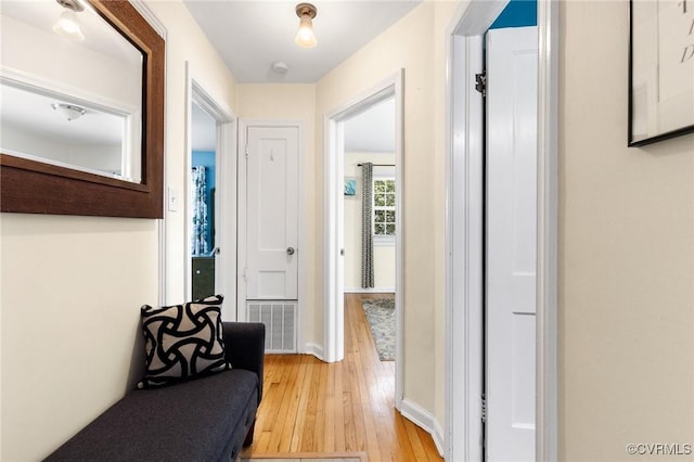 hallway featuring visible vents, light wood finished floors, and baseboards
