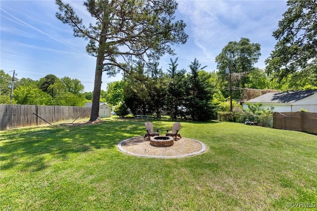 view of yard featuring a storage unit, a fenced backyard, an outdoor fire pit, and an outbuilding