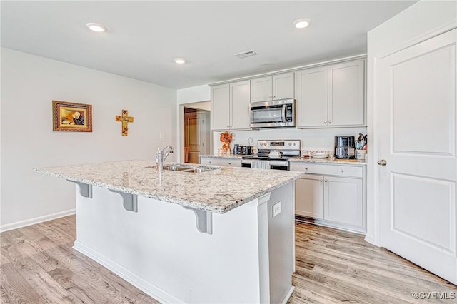 kitchen featuring light stone counters, a sink, a kitchen breakfast bar, an island with sink, and stainless steel appliances