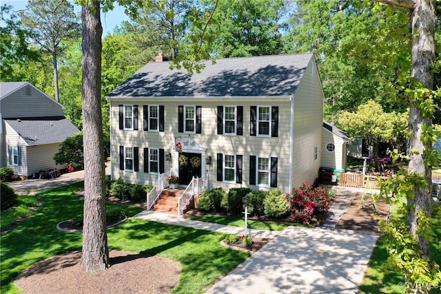 colonial house featuring a shingled roof and a front yard