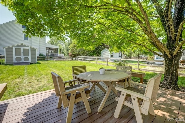 wooden deck featuring an outdoor structure, fence, a lawn, a storage shed, and outdoor dining space