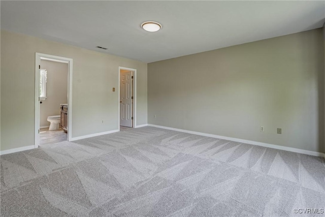 unfurnished bedroom with baseboards, visible vents, ensuite bath, and light colored carpet