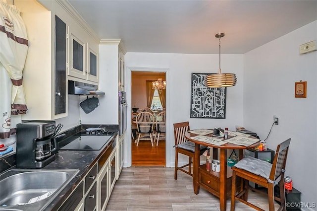kitchen featuring pendant lighting, oven, glass insert cabinets, black electric stovetop, and under cabinet range hood