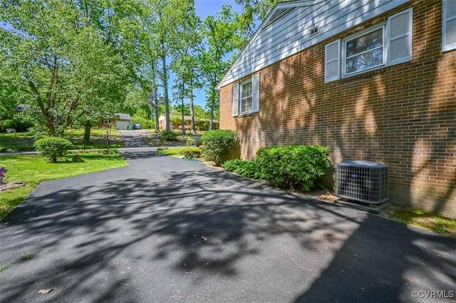 view of property exterior featuring central air condition unit, brick siding, and driveway