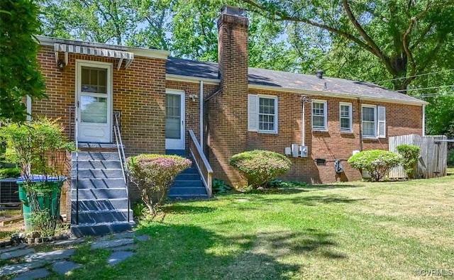 rear view of property with a lawn, a chimney, roof with shingles, and brick siding