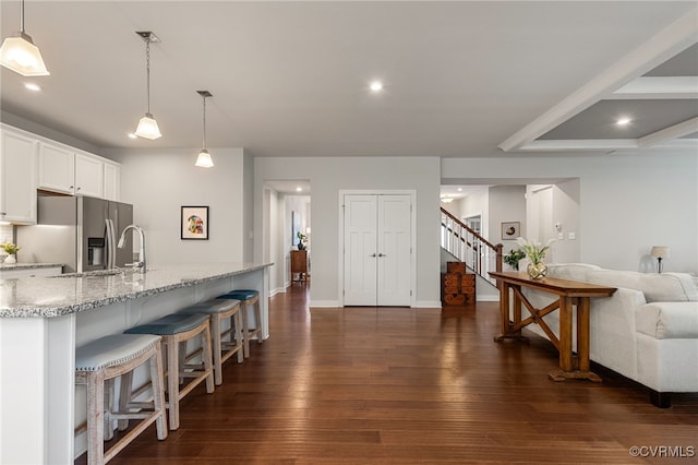 kitchen with light stone counters, open floor plan, stainless steel fridge, a breakfast bar, and dark wood-type flooring
