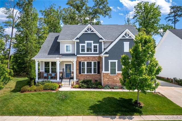 craftsman-style home featuring a porch, a shingled roof, a front yard, and brick siding