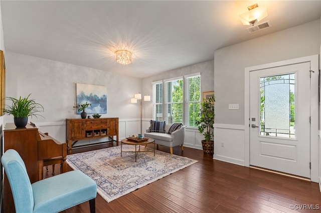 living area with visible vents, dark wood finished floors, a decorative wall, and wainscoting