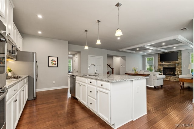 kitchen with white cabinets, a sink, a kitchen island with sink, a stone fireplace, and stainless steel appliances