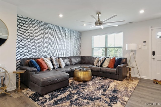 living room featuring a ceiling fan, baseboards, wood finished floors, and an accent wall