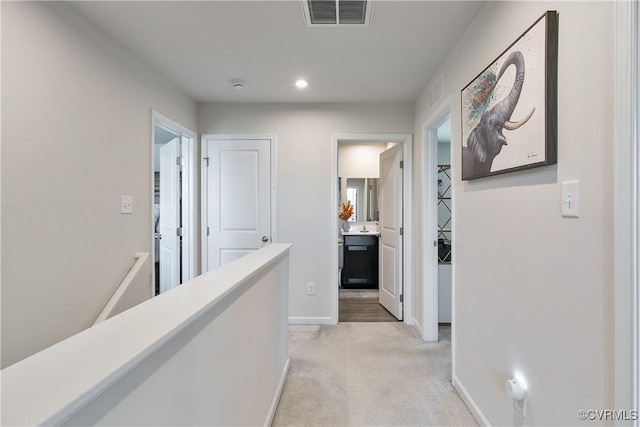 hallway with visible vents, recessed lighting, baseboards, and light colored carpet