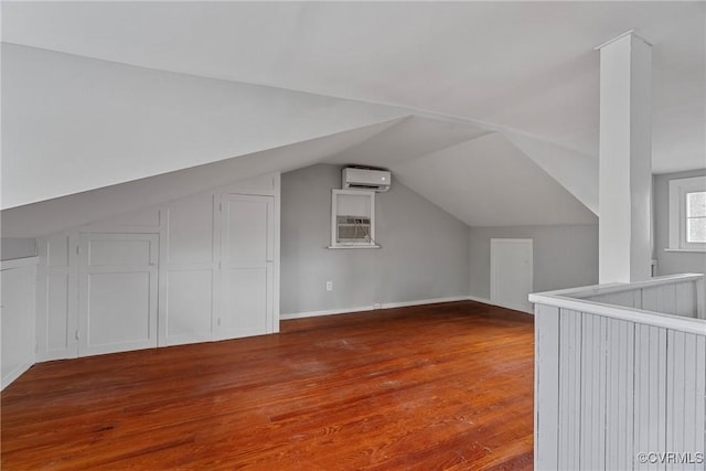 additional living space with an AC wall unit, lofted ceiling, and wood finished floors