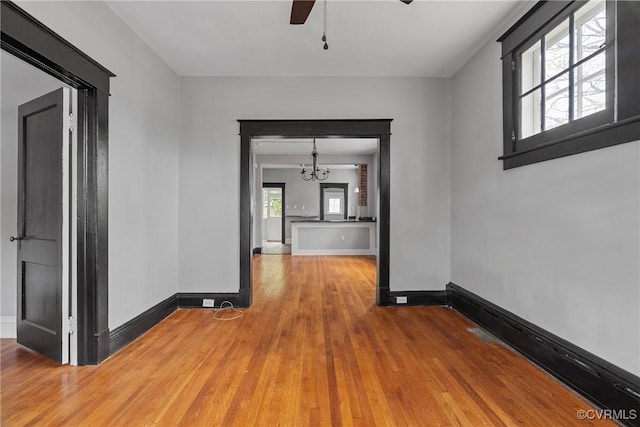 unfurnished room with baseboards, wood finished floors, and ceiling fan with notable chandelier