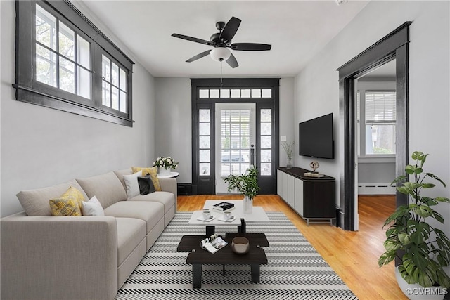 living room featuring baseboard heating, a ceiling fan, and light wood finished floors