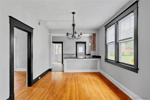 unfurnished dining area with light wood-style floors, baseboards, and an inviting chandelier