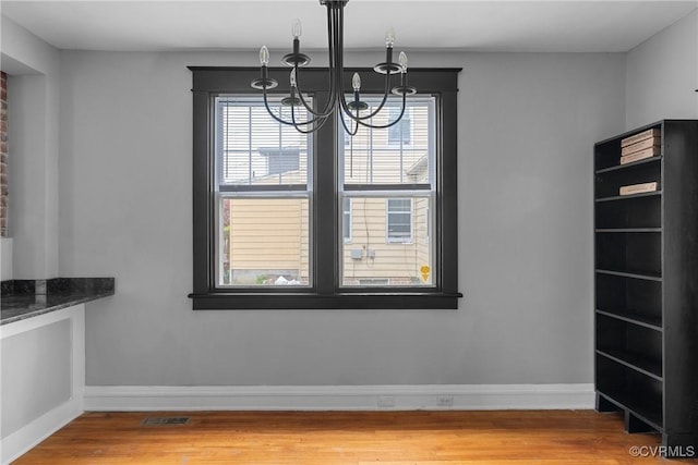 unfurnished dining area featuring an inviting chandelier, baseboards, light wood finished floors, and visible vents