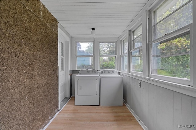 clothes washing area featuring laundry area, light wood-style floors, washer and dryer, and wooden walls