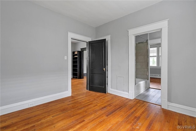unfurnished bedroom featuring wood-type flooring, baseboards, and baseboard heating