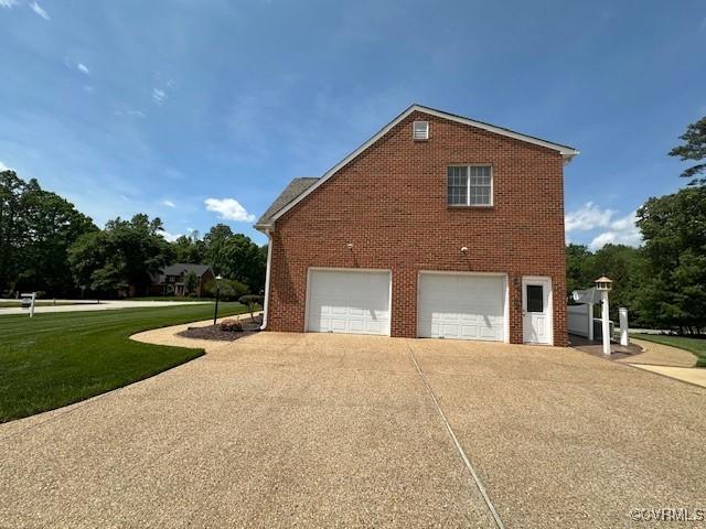 view of property exterior featuring an attached garage, a yard, brick siding, and concrete driveway