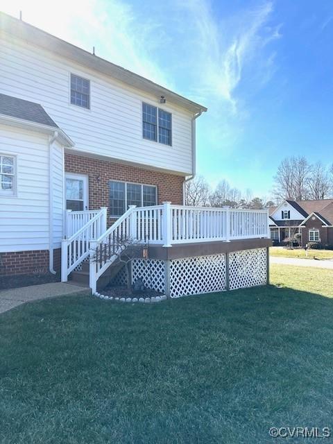 back of house featuring a lawn, brick siding, and a deck