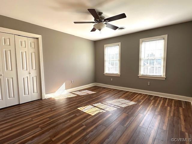 unfurnished bedroom featuring a closet, visible vents, baseboards, a ceiling fan, and dark wood finished floors