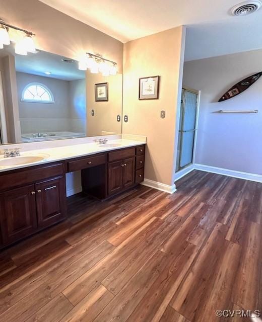 bathroom featuring visible vents, double vanity, a shower with door, wood finished floors, and a sink