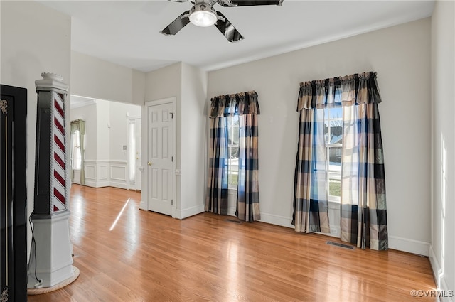 empty room with decorative columns, a ceiling fan, light wood-style flooring, and visible vents
