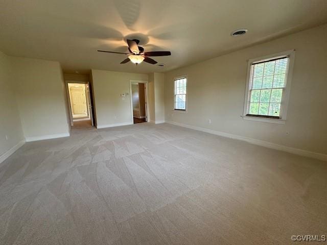 empty room with light colored carpet, a ceiling fan, baseboards, and visible vents