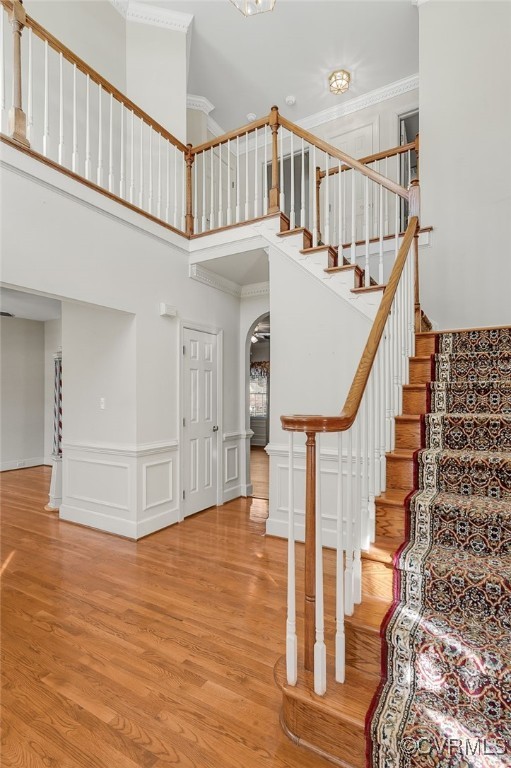 staircase featuring arched walkways, a high ceiling, wood finished floors, and ornamental molding
