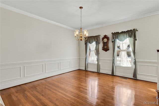 spare room with visible vents, ornamental molding, wood finished floors, a wainscoted wall, and a notable chandelier
