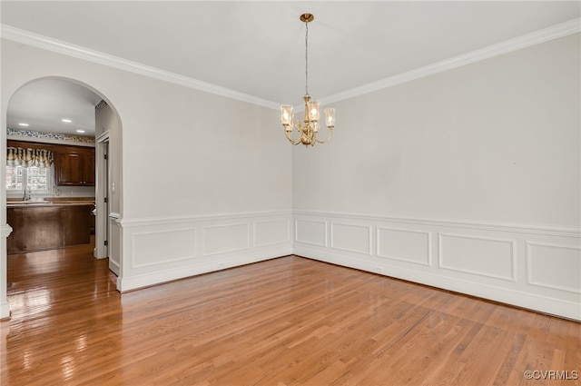 empty room with crown molding, wainscoting, light wood-style floors, arched walkways, and a chandelier