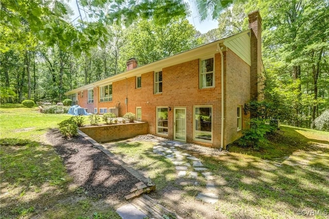 rear view of property featuring a chimney, brick siding, and a lawn
