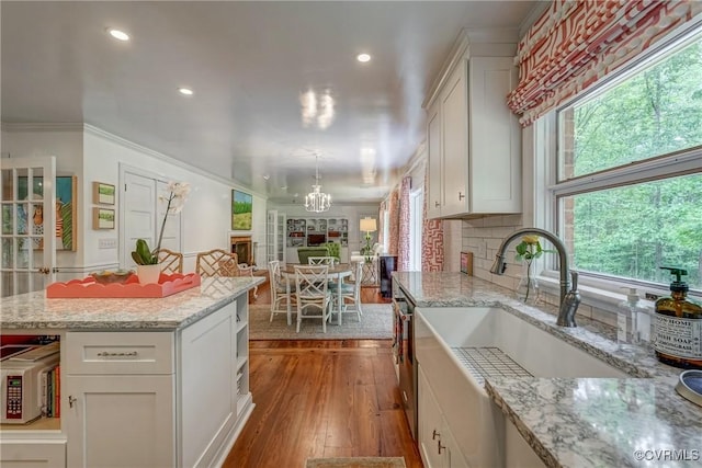 kitchen with a chandelier, a sink, wood-type flooring, crown molding, and white cabinetry
