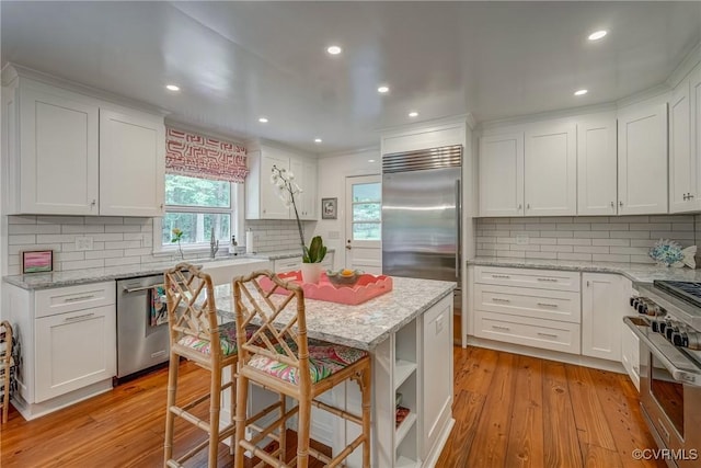 kitchen with high quality appliances, white cabinets, tasteful backsplash, light wood finished floors, and recessed lighting