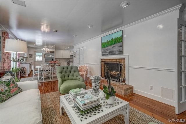 living area with a brick fireplace, a chandelier, wood finished floors, ornamental molding, and baseboards