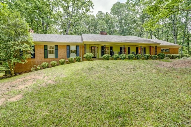 single story home with a chimney, a front yard, view of wooded area, and brick siding