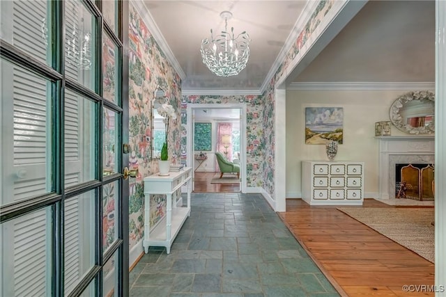 hall with ornamental molding, baseboards, a chandelier, stone tile floors, and wallpapered walls