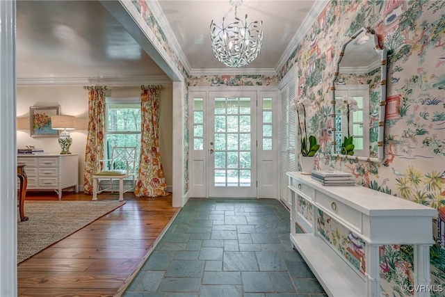 doorway to outside with ornamental molding, a chandelier, baseboards, wallpapered walls, and stone tile floors