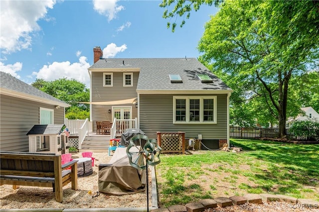 rear view of property featuring a deck, fence, a fire pit, a yard, and a chimney