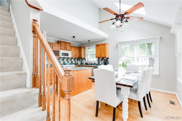 dining space with a ceiling fan, vaulted ceiling, light wood-style floors, and stairway