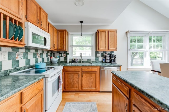 kitchen with a sink, dark countertops, pendant lighting, white appliances, and light wood-style floors