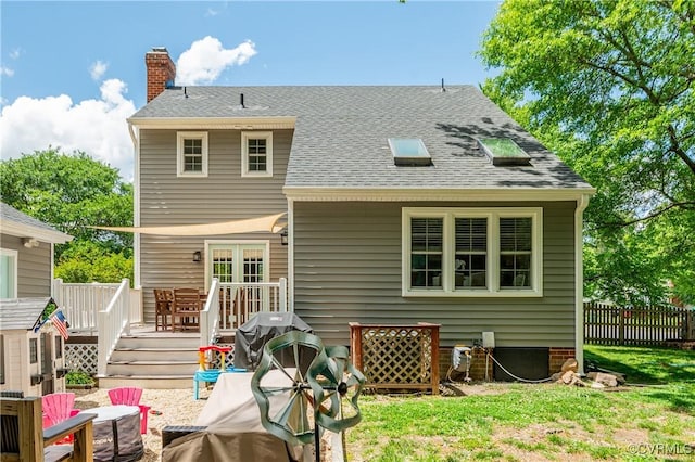 rear view of house with a chimney, a deck, a shingled roof, and fence