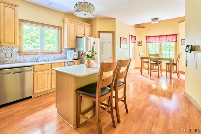 kitchen with light brown cabinetry, appliances with stainless steel finishes, light countertops, light wood-type flooring, and a kitchen bar